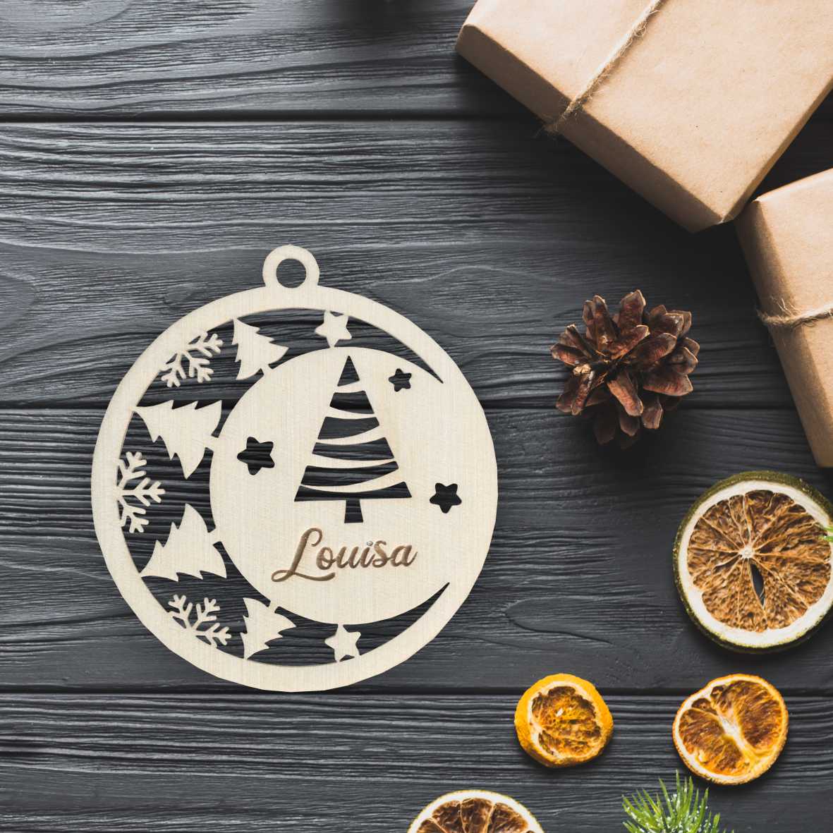 Holz-Weihnachtskugel mit Bäumen auf Holztisch neben Geschenk und getrockneten Orangen