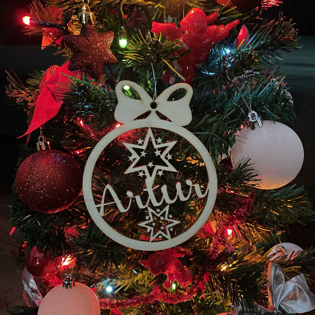 Holz-Weihnachtskugel mit Sternmotiv und Name Artur vor roter Weihnachtsdekoration