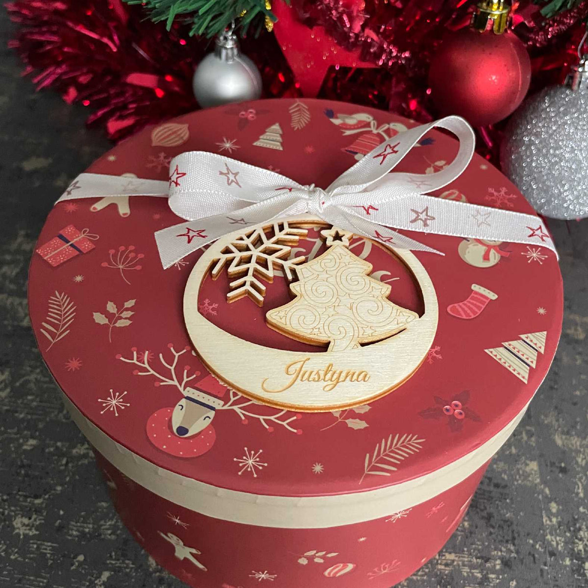 Holz-Weihnachtskugel mit Tannenbaum auf einer roten Geschenkbox mit Schleife
